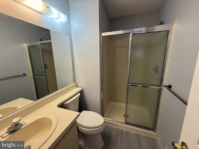 bathroom featuring vanity, a textured ceiling, a shower with door, hardwood / wood-style flooring, and toilet