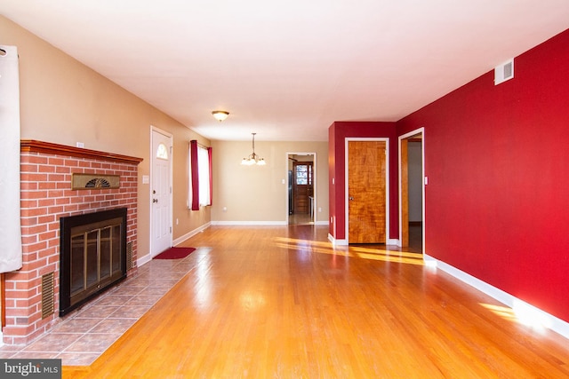 unfurnished living room with a brick fireplace, an inviting chandelier, and wood-type flooring