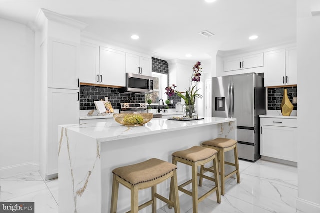 kitchen with a center island, stainless steel appliances, decorative backsplash, a breakfast bar area, and white cabinetry