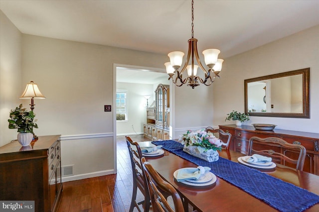 dining area with dark wood-type flooring and an inviting chandelier