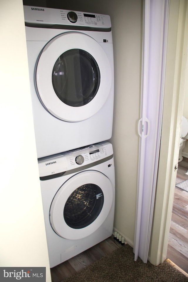 laundry area with hardwood / wood-style flooring and stacked washer and clothes dryer