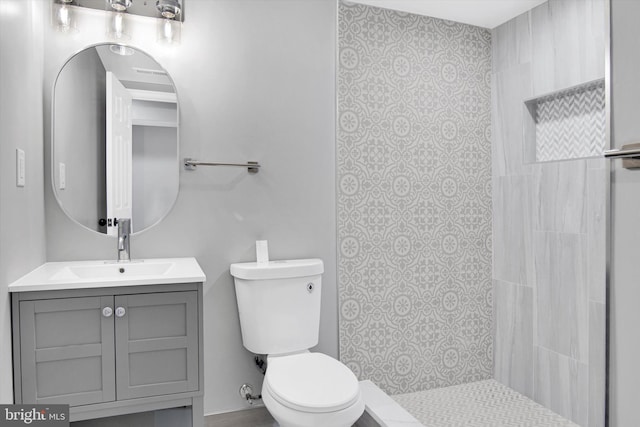 full bathroom featuring toilet, a tile shower, and vanity