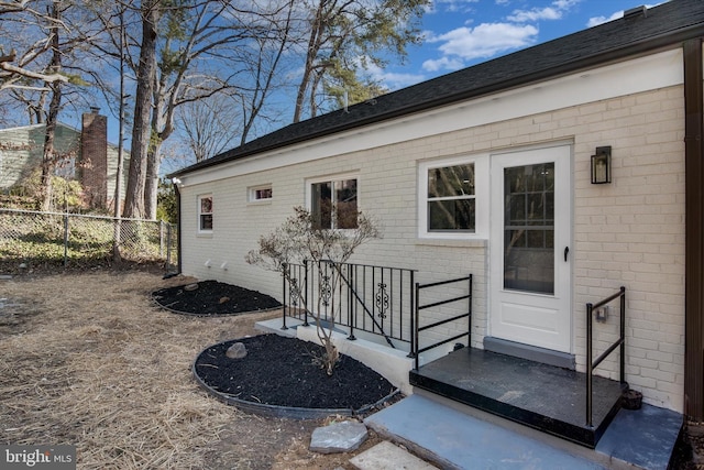 view of exterior entry with brick siding and fence