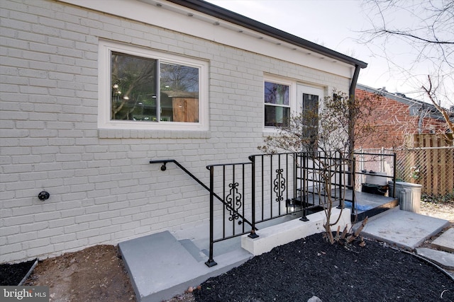 doorway to property featuring brick siding and fence