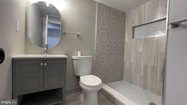 bathroom featuring vanity, a tile shower, and toilet