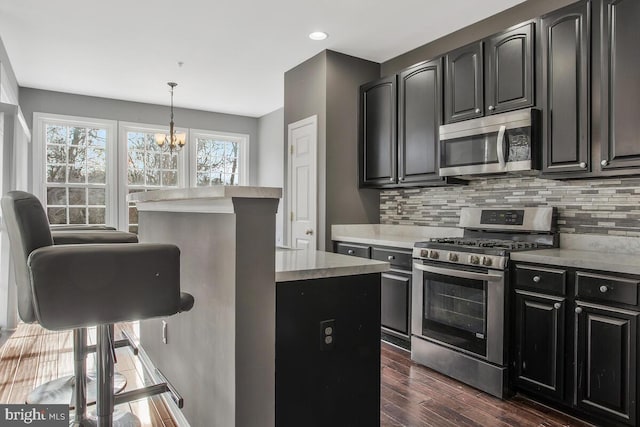 kitchen with appliances with stainless steel finishes, backsplash, dark hardwood / wood-style flooring, a notable chandelier, and hanging light fixtures