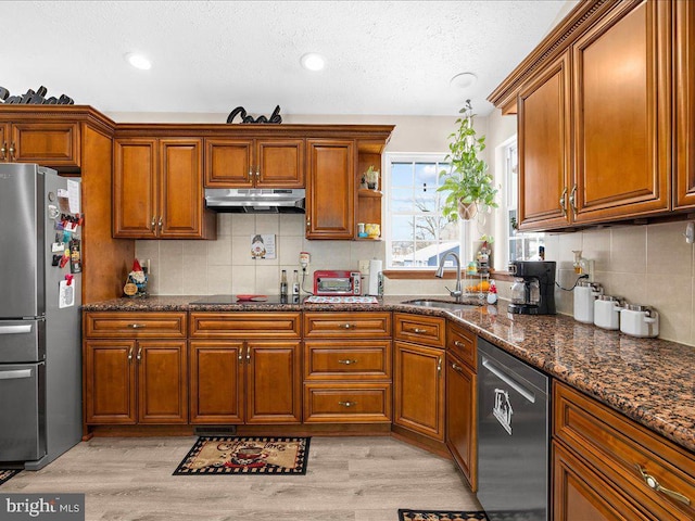 kitchen with dark stone counters, appliances with stainless steel finishes, sink, and light hardwood / wood-style floors