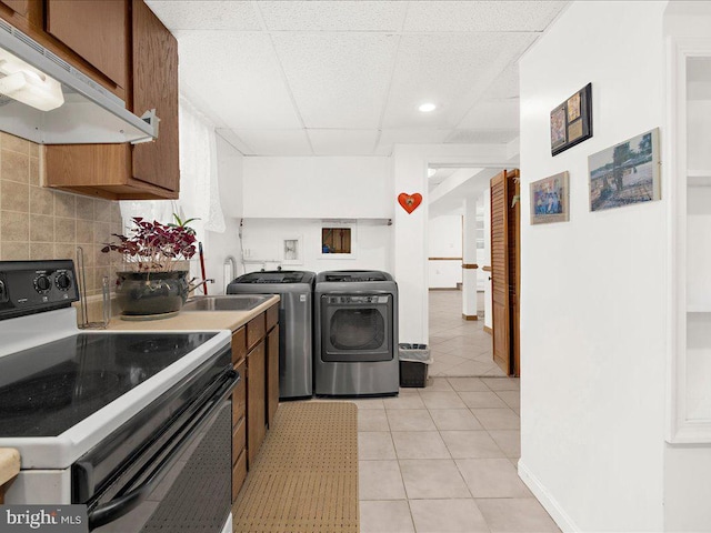 kitchen with light tile patterned floors, tasteful backsplash, electric range, a paneled ceiling, and washing machine and dryer