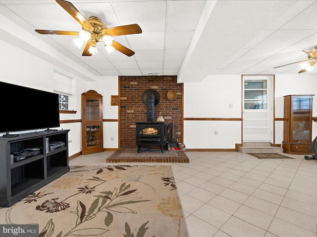 tiled living room with ceiling fan, a wood stove, and a drop ceiling