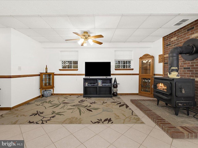 living room with ceiling fan, tile patterned flooring, a wood stove, and a drop ceiling