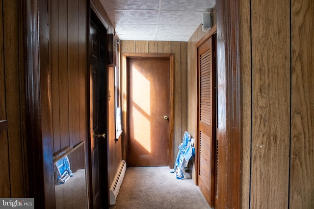 hallway featuring carpet flooring, wood walls, and a baseboard heating unit