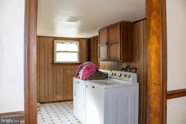 clothes washing area with separate washer and dryer, wooden walls, and cabinets