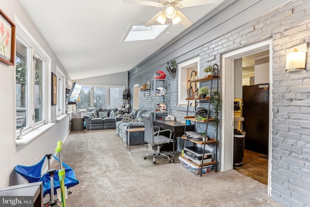 home office featuring vaulted ceiling with skylight, ceiling fan, carpet floors, and brick wall