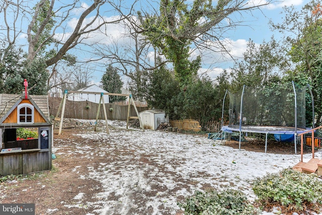 yard covered in snow featuring a trampoline and a storage unit