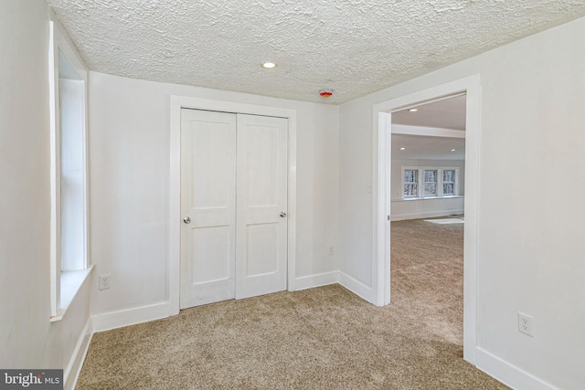 unfurnished bedroom featuring a textured ceiling, light colored carpet, and a closet