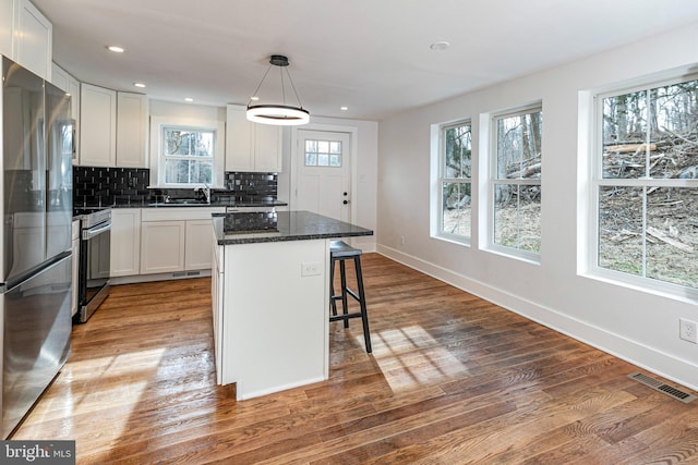 kitchen featuring a center island, dark stone counters, white cabinets, decorative light fixtures, and stainless steel appliances