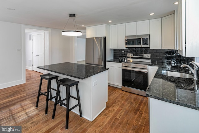 kitchen with appliances with stainless steel finishes, a kitchen island, white cabinetry, sink, and hanging light fixtures