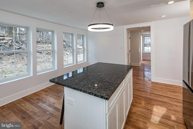 kitchen with a kitchen island, dark wood-type flooring, white cabinetry, dark stone countertops, and hanging light fixtures