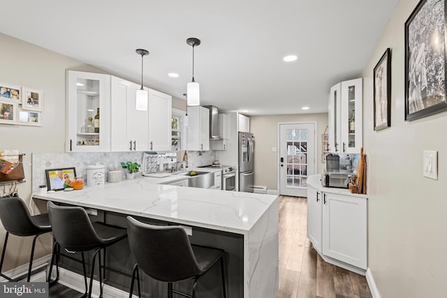 kitchen with white cabinets, wall chimney exhaust hood, kitchen peninsula, and stainless steel appliances