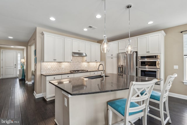 kitchen featuring dark stone counters, stainless steel appliances, sink, a center island with sink, and white cabinetry