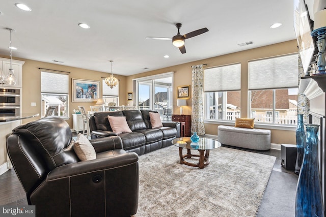 living room with a wealth of natural light, a fireplace, dark hardwood / wood-style floors, and ceiling fan with notable chandelier