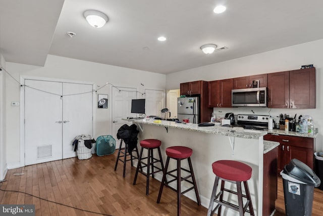 kitchen featuring dark wood-type flooring, stainless steel appliances, a breakfast bar, and a center island with sink