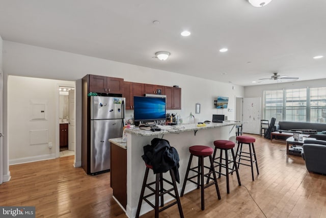 kitchen featuring stainless steel refrigerator, an island with sink, a kitchen breakfast bar, light stone counters, and light hardwood / wood-style floors