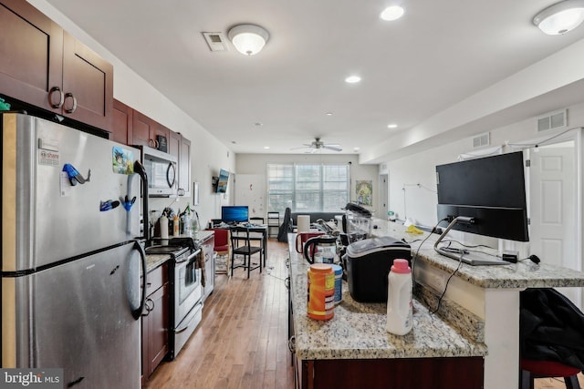 kitchen featuring a breakfast bar area, light stone counters, ceiling fan, stainless steel appliances, and light hardwood / wood-style floors