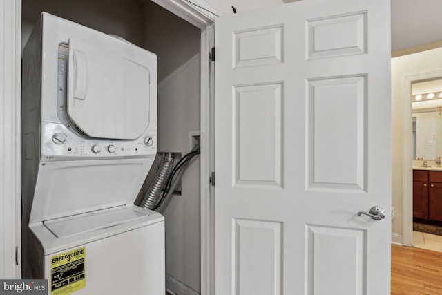 clothes washing area featuring stacked washer and dryer, sink, and light wood-type flooring