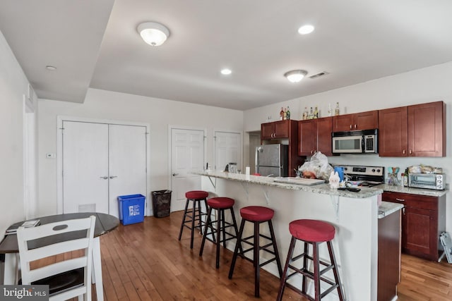 kitchen with a breakfast bar, dark hardwood / wood-style floors, a kitchen island with sink, stainless steel appliances, and light stone countertops