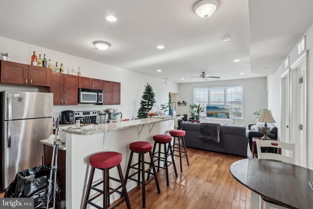 kitchen featuring a kitchen island, appliances with stainless steel finishes, a breakfast bar, light stone counters, and light hardwood / wood-style floors