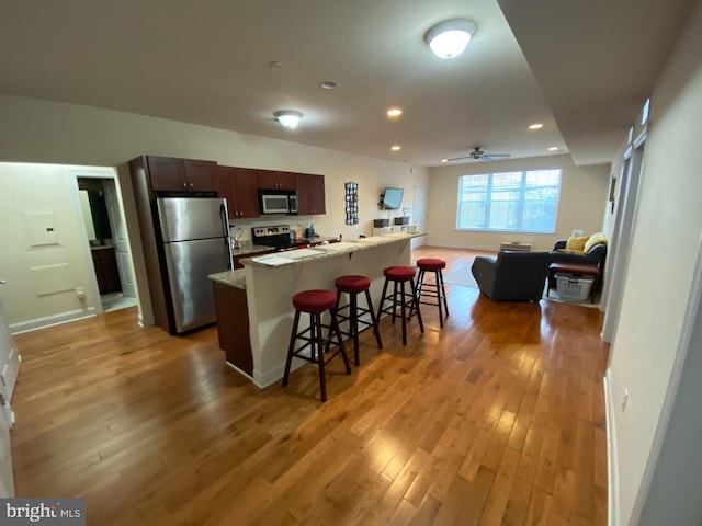 kitchen featuring a kitchen island, appliances with stainless steel finishes, a breakfast bar area, dark brown cabinetry, and light wood-type flooring