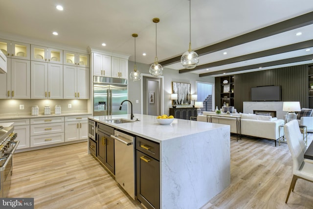 kitchen with high end appliances, white cabinets, a sink, and light wood-type flooring