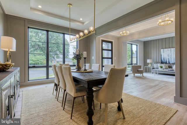 dining area with a tray ceiling, recessed lighting, an inviting chandelier, and light wood-style floors