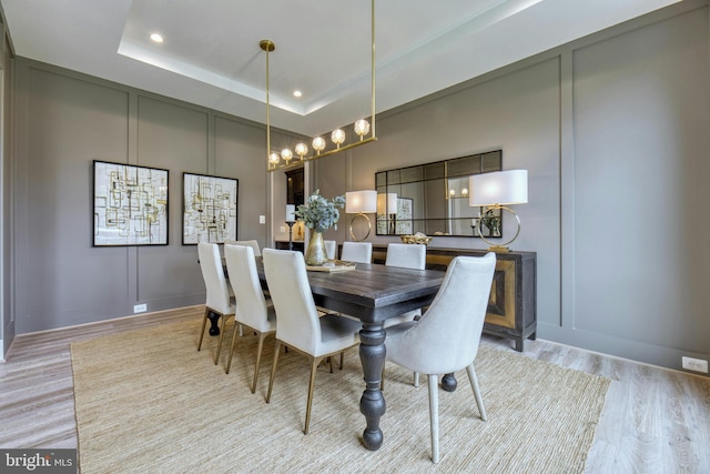 dining area featuring light wood-type flooring, recessed lighting, a decorative wall, and a raised ceiling