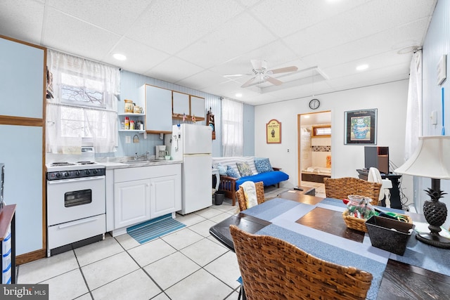 kitchen with a drop ceiling, white appliances, ceiling fan, light tile patterned floors, and white cabinetry