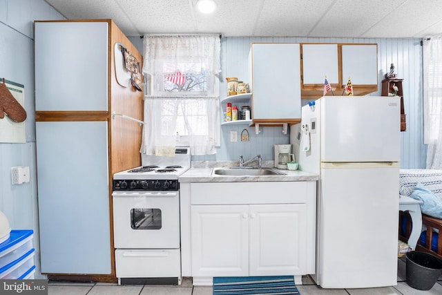 kitchen with a paneled ceiling, white appliances, sink, light tile patterned floors, and white cabinetry