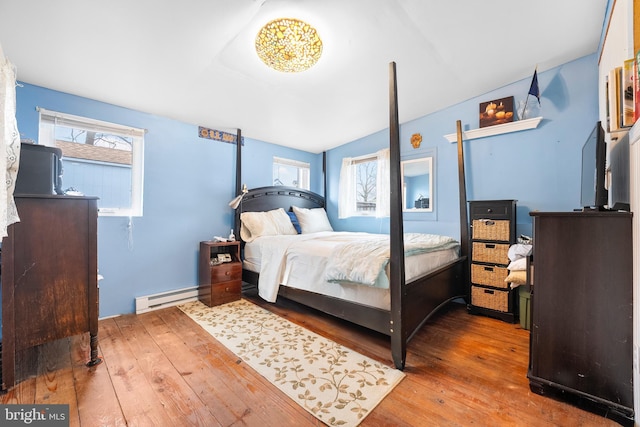 bedroom with hardwood / wood-style flooring, a baseboard radiator, and multiple windows