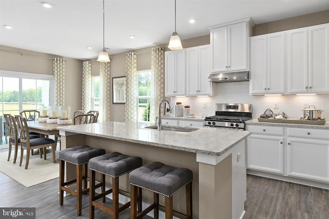 kitchen with stainless steel stove, white cabinetry, sink, hanging light fixtures, and a kitchen island with sink