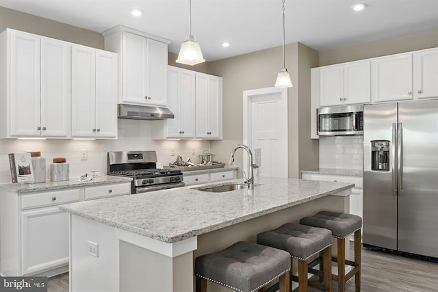 kitchen with sink, white cabinetry, stainless steel appliances, an island with sink, and decorative light fixtures