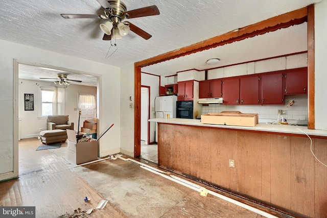 kitchen featuring kitchen peninsula, decorative backsplash, ceiling fan, white fridge, and black oven