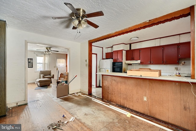 kitchen with ceiling fan, white refrigerator, kitchen peninsula, black oven, and decorative backsplash