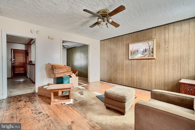 living room featuring wood walls, light hardwood / wood-style flooring, ceiling fan, and a textured ceiling