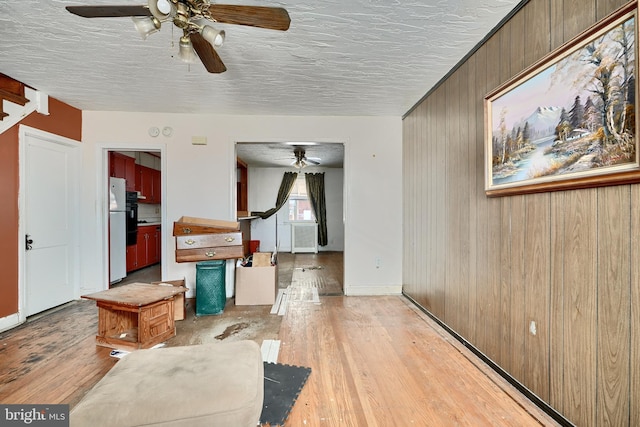 living room featuring a textured ceiling, light wood-type flooring, and wood walls