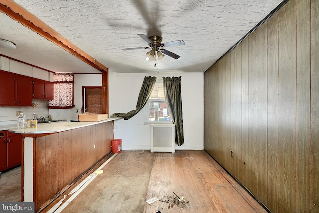 kitchen with kitchen peninsula, radiator, a textured ceiling, ceiling fan, and wood walls