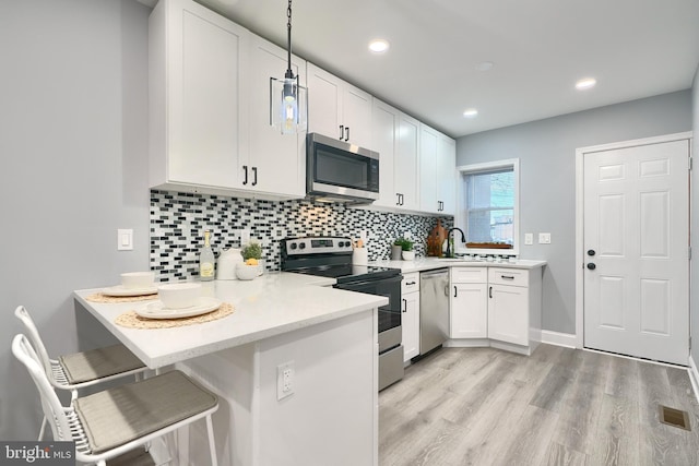 kitchen featuring hanging light fixtures, stainless steel appliances, kitchen peninsula, a kitchen bar, and white cabinets