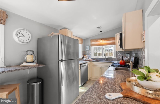 kitchen with lofted ceiling, stainless steel appliances, dark stone counters, sink, and hanging light fixtures