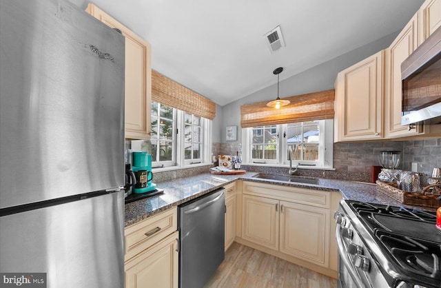 kitchen featuring stainless steel appliances, dark stone counters, vaulted ceiling, pendant lighting, and sink