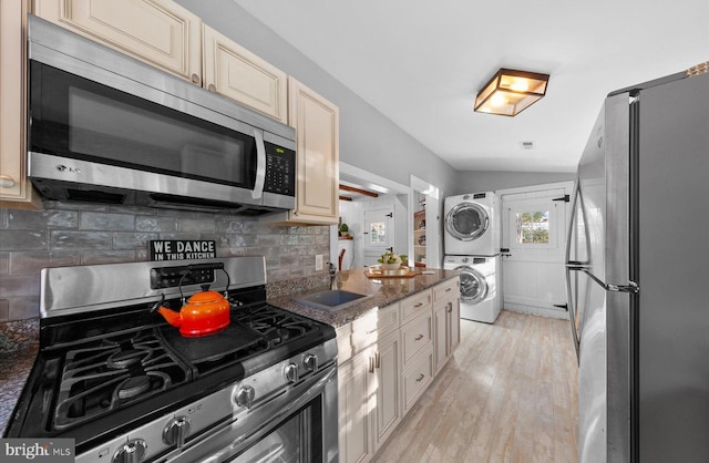 kitchen with lofted ceiling, dark stone countertops, sink, stacked washer / dryer, and appliances with stainless steel finishes