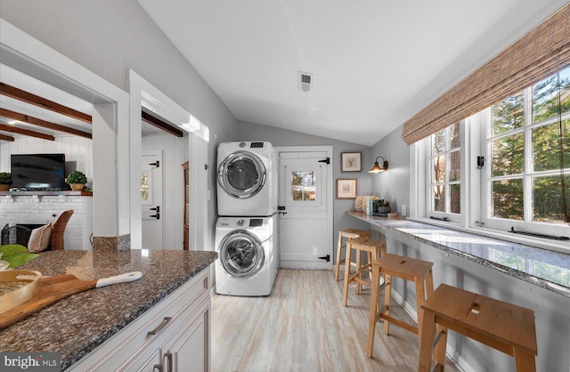 clothes washing area featuring stacked washer / drying machine, a healthy amount of sunlight, and light wood-type flooring